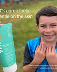 A boy smiling at a sports field holding a Thinkkids SPF 50 sunscreen tube with text overlay saying '97% agree feels gentle on the skin.