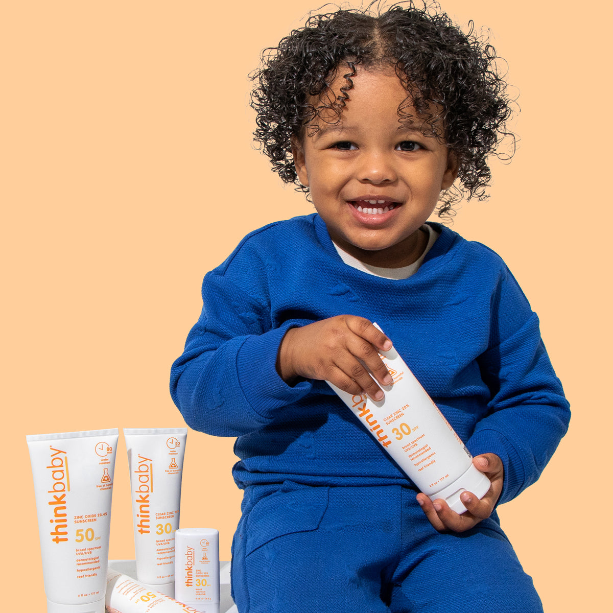 Smiling child holding ThinkBaby Clear Zinc 30 SPF Sunscreen, emphasizing safe and effective sun protection for kids.