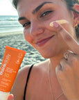 Woman applying ThinkDaily Tinted Face 30 SPF Sunscreen on the beach, emphasizing broad-spectrum UV protection, dermatologist recommended, and reef-friendly formula.