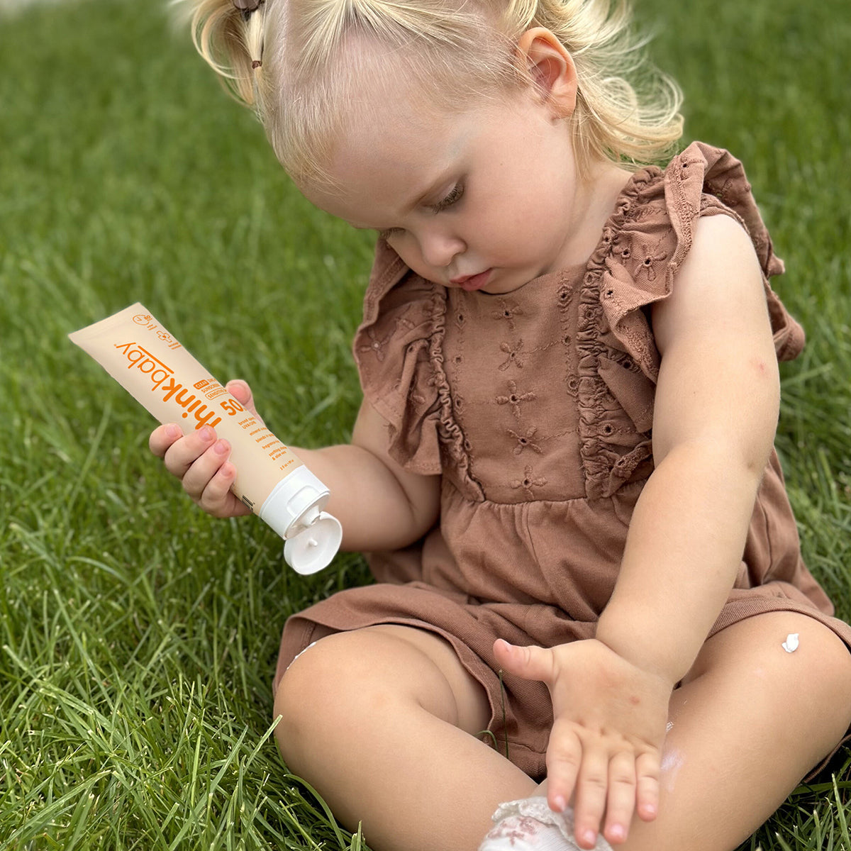 Thinkbaby sunscreen applied outdoors on grass, showing gentle mineral sunscreen suitable for little ones with easy application and skin‑friendly formula.